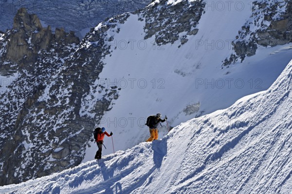 Two mountaineers run across a snow-covered mountain ridge, Aiguille du Midi, Chamonix-Mont-Blanc,