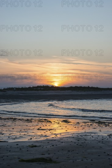 Sunset on a quiet beach with soft light on the waves, wet beach at low tide, dunes in the