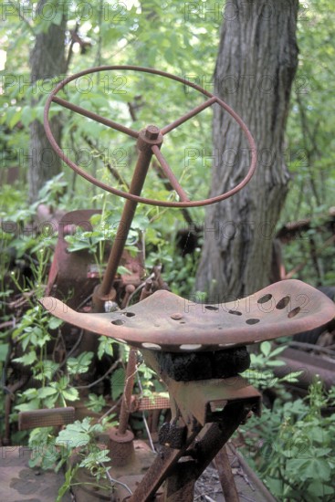 Rusted wheel and iron seat from an American tractor around 1900, deposited in a wooded area,