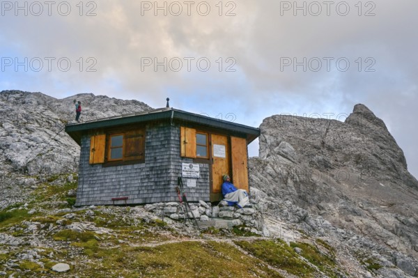 Two mountaineers relax at the Wildalmkirchl bivouac with the Wildalmkirchl summit in the