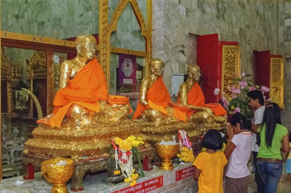 Buddhist believers Buddhists pray making offerings to statues of Buddhist monks covered with gold