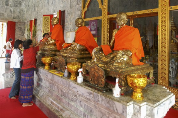 Buddhist believers Buddhists pray making offerings to statues of Buddhist monks covered with gold