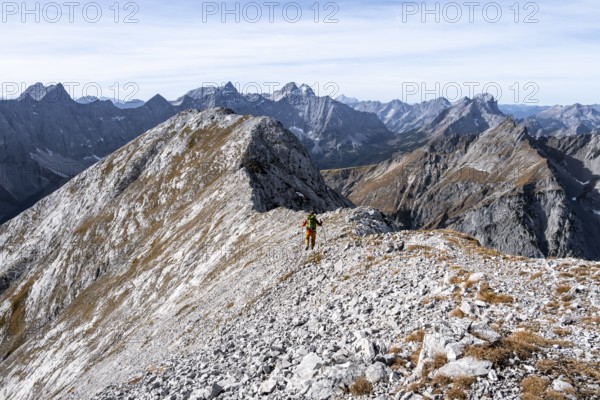 Hikers on the summit ridge of the Gamsjoch, behind rock faces of the Laliderer Spitze, eastern