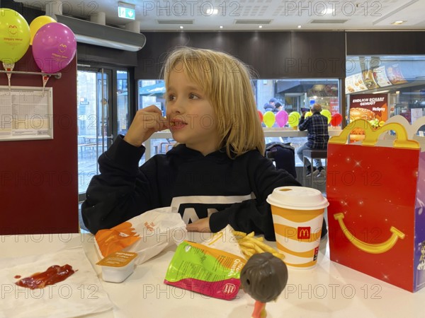 Interior view, child, boy, 7 years, blonde, eating Happy Meal, children's menu, at McDonald's