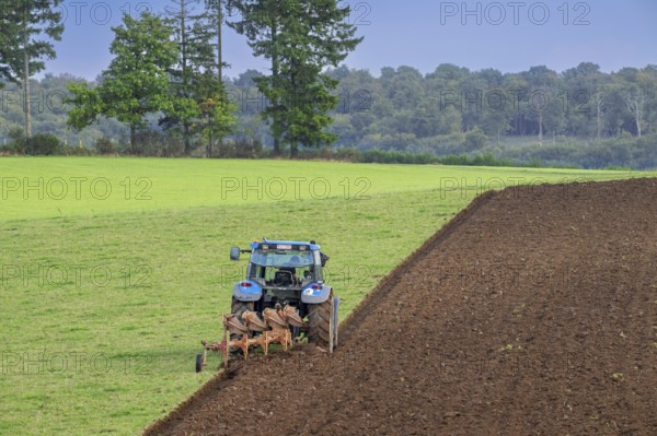 Tractor with plough, agricultural ploughing machine working on a field in autumn, fall in the