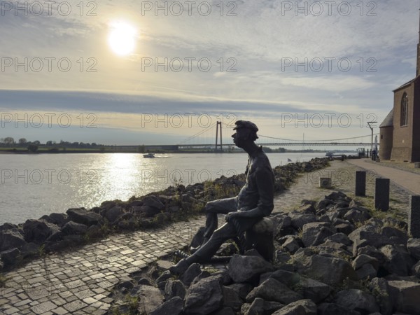 Photo with melancholy mood of bronze sculpture Poortekerl looking at Rhine waiting for ship to