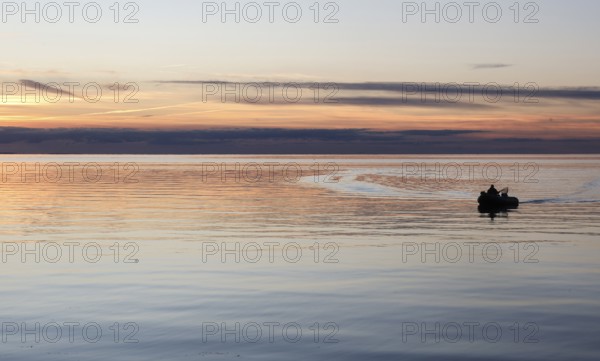 Angler on the beach during sunset, an angler docks on the shore with his inflatable boat and dog,