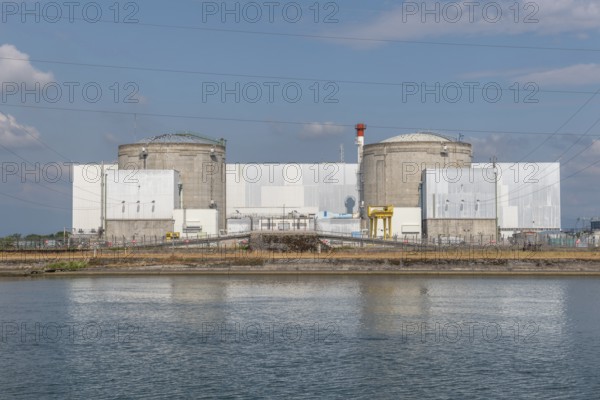 A large industrial nuclear power plant is located on a quiet water front. Two tall cylindrical