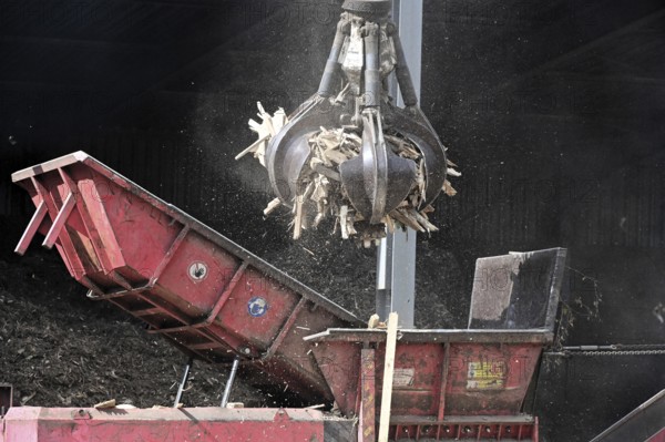 Loading crane with grab arm for loading wood waste for wood pellet production on the premises of