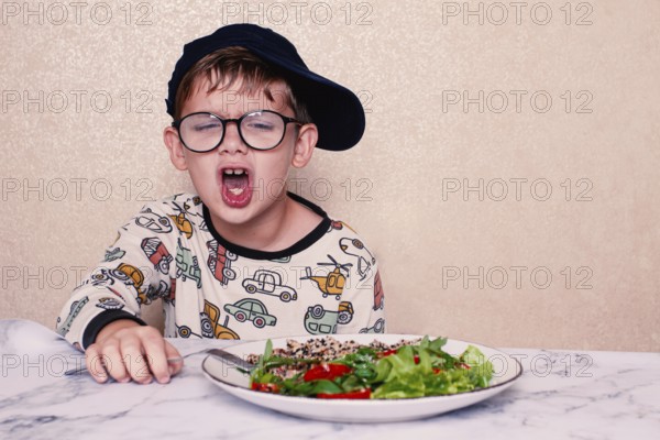 Child reacts dramatically to a salad served on a marble table at home during lunchtime, A little