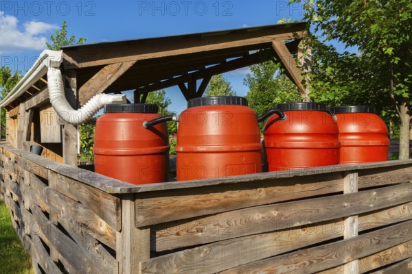 Reddish brown plastic water butts collecting and storing rain water from white plastic downspout in