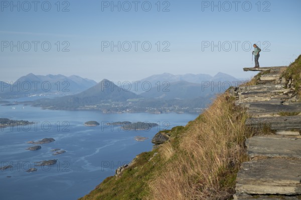Woman with walking sticks standing on a ledge, Rørsethornet stone stairs, with 3292 steps one of