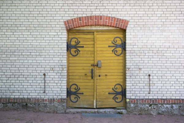 Yellow wooden door with wrought-iron fittings, white brick wall, former paper mill for the