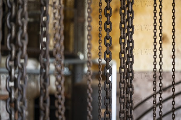 Hanging iron chains in various sizes, factory hall with machines for the production of cardboard