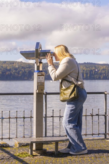 Woman looking through binoculars with a lake in the background, Überlingen, Lake Constance, Germany