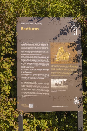 Information board about the Badturm with historical text and map, surrounded by green plants,