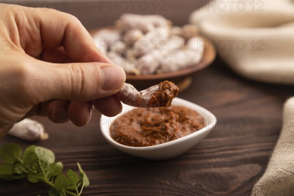 Small smoked Chicken sausages in wooden bowl with hand on brown wooden background and linen textile