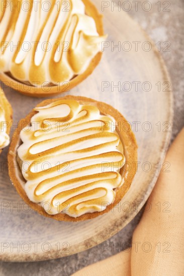 French lemon tart with meringue on brown concrete background, cup of coffee, orange linen textile,