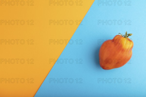 Red Heart Shape tomato on blue and orange pastel paper background. Top view, flat lay, copy space.