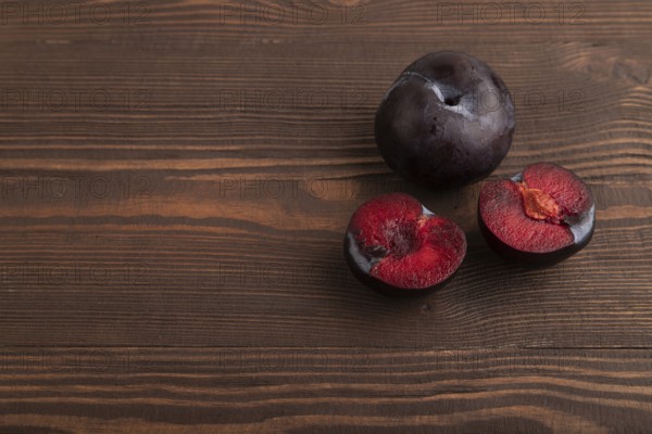 Purple Plum Cut in half on brown wooden background. Side view, copy space. healthy food, vegetable,