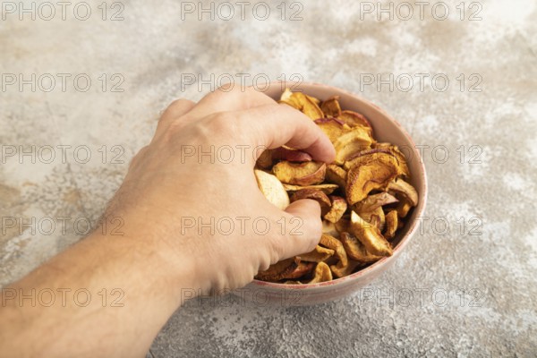 Dried Apples in ceramic bowl with hand on brown concrete background. Side view, copy space, flat