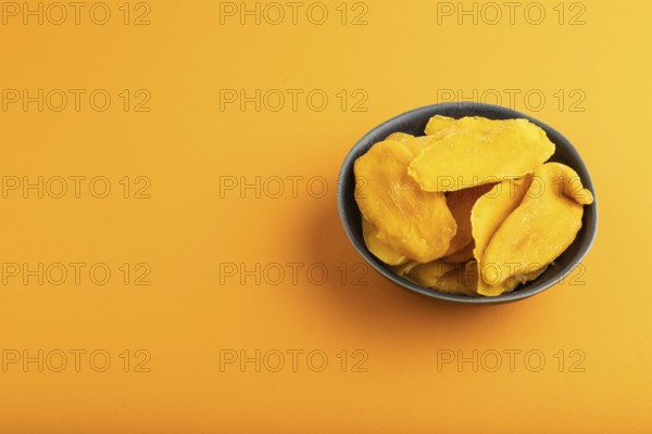Dried Mango in blue ceramic bowl on orange pastel paper background. Side view, copy space. healthy