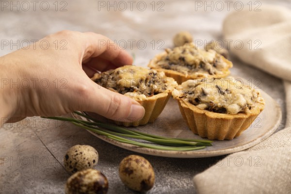 Tartlets with meat and cheese with hand on brown concrete background and linen textile. side view,