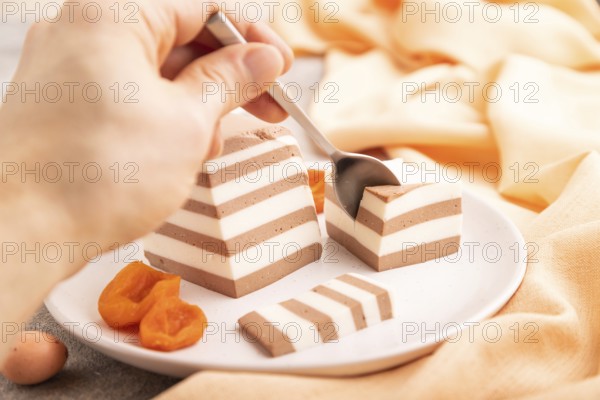Cocoa and milk jelly with dried apricots with hand on brown concrete background and orange textile,