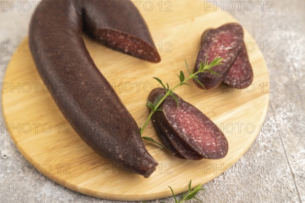 Sujuk sausage on wooden cutting board with pepper and herbs on brown concrete background. Side