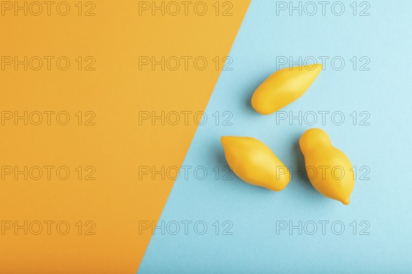Yellow tomatoes on blue and orange pastel paper background. Top view, copy space, flat lay. healthy