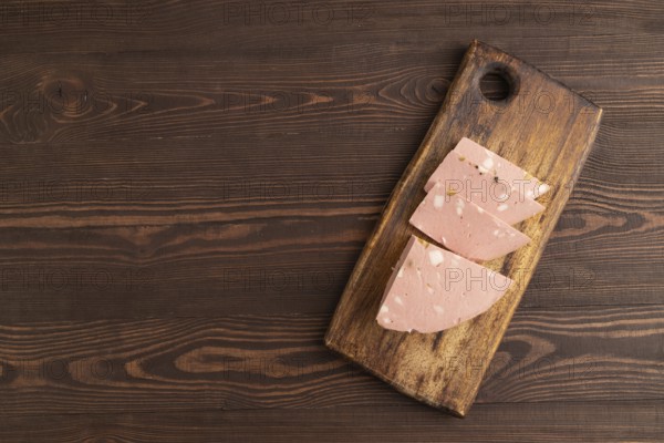 Mortadella sausage on wooden cutting board with pepper and herbs on brown wooden background. Top