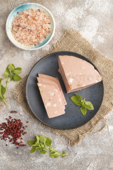 Mortadella sausage on plate with pepper and herbs on brown concrete background and linen textile.