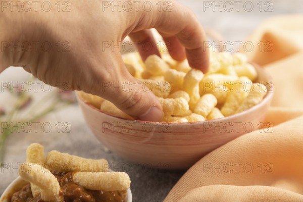 Corn flakes sticks with hand with caramel in ceramic bowl on gray concrete background and orange