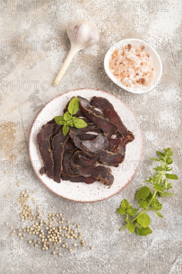 Armenian Basturma dried meat on plate with pepper and herbs on brown concrete background. Top view,