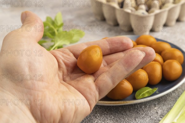 Pile of Smoked Quail eggs on plate with hand on a brown concrete background. side view, close up