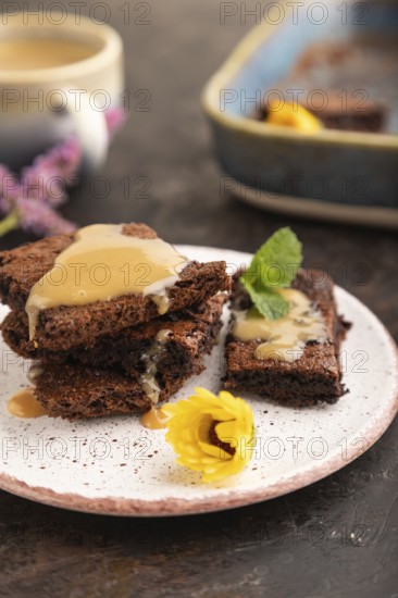 Chocolate brownie with caramel sauce with a cup of coffee on black concrete background. side view,