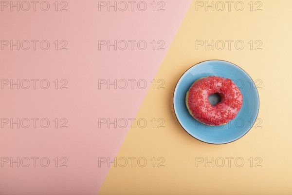 Pink Donut with sprinkles on blue ceramic plate on blue and orange pastel paper background, top