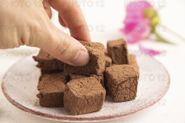 Chocolate marshmallow with cup of coffee with hand on white wooden background. side view, close up,