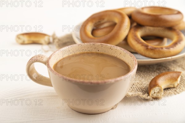 Homemade Ring Bagel with cup of coffee on white wooden background and linen textile. side view,