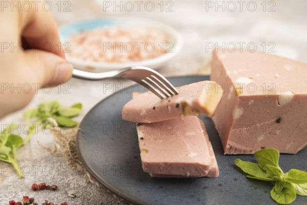 Mortadella sausage with hand on plate with pepper and herbs on brown concrete background and linen