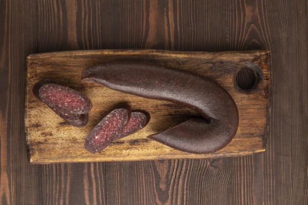 Sujuk sausage on wooden cutting board with pepper and herbs on brown wooden background. Top view,