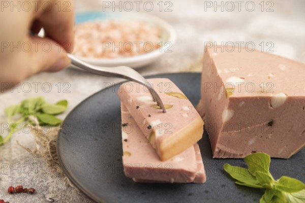 Mortadella sausage with hand on plate with pepper and herbs on brown concrete background and linen