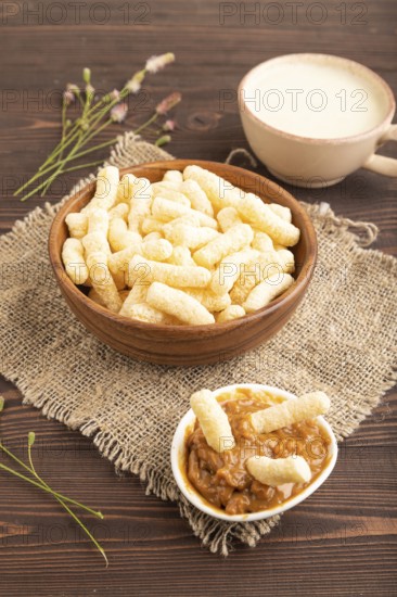 Corn flakes sticks with caramel in wooden bowl on brown wooden background and linen textile. Side