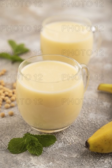 Organic non dairy banana and soy milk in glass on brown concrete background. Vegan healthy food