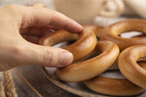 Homemade Ring Bagel with hand with cup of coffee on brown concrete background and linen textile.