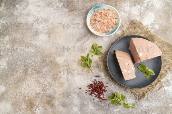 Mortadella sausage on plate with pepper and herbs on brown concrete background and linen textile.