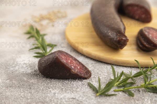 Sujuk sausage on wooden cutting board with pepper and herbs on brown concrete background. Side