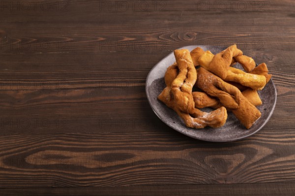Crunchy biscuit Brushwood cookies sprinkled with powdered sugar on brown wooden background, side