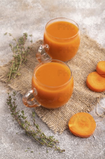 Two glasses with carrot juice, on brown concrete background and linen textile. Diet, healthy eating