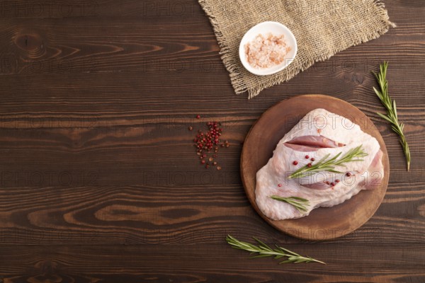 Raw Turkey Thigh with spices and rosemary on cutting board on brown wooden background and linen
